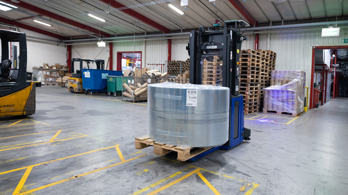 Gaffeltruck flytter palle med stor indpakket stålrulle i lagerhal med paller og industrimaterialer